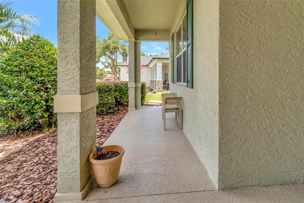 A covered front porch features a beige stucco finish, a potted plant, and a chair — 3507 ARLINGTON RIDGE BOULEVARD, LEESBURG, FL