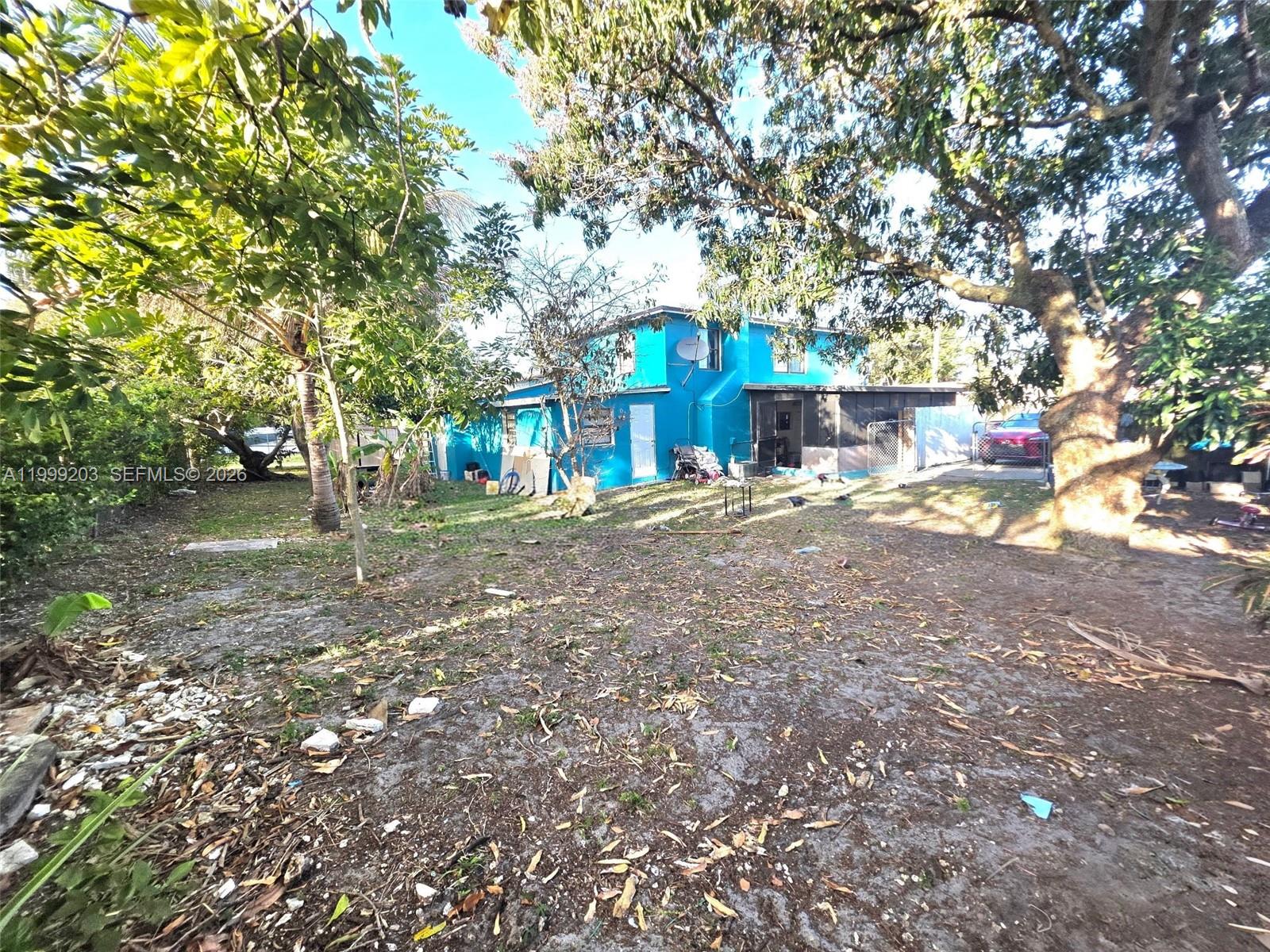 A bright blue two-story house stands behind a large, tree-shaded dirt yard — 720 SW 7th Ter, Hallandale Beach FL 33009, HALLANDALE BEACH, FL