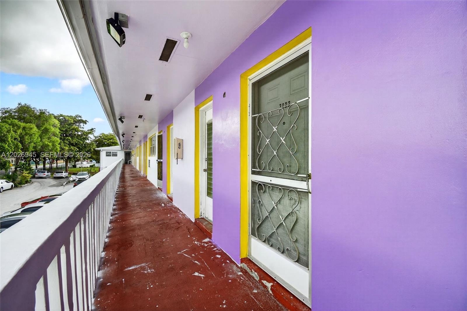 An outdoor walkway with purple walls, yellow door frames, and a red floor — 245 NE 191st St # 3022, Miami FL 33179, MIAMI, FL