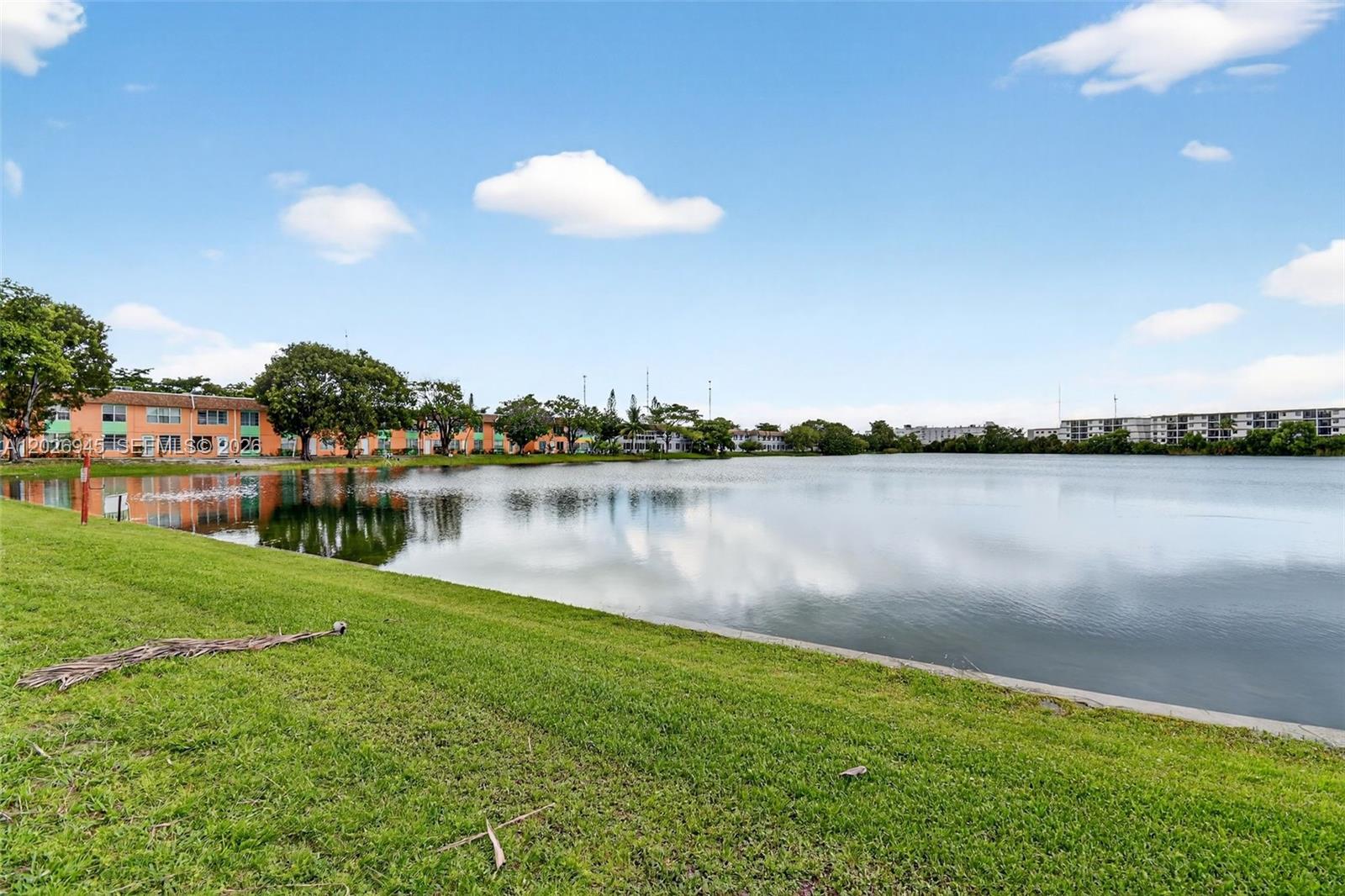 A grassy lawn slopes down to a lake with apartment buildings in the background — 245 NE 191st St # 3022, Miami FL 33179, MIAMI, FL