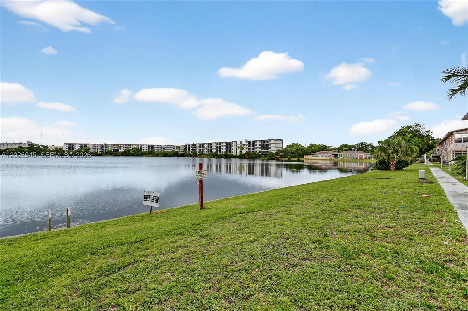 A grassy lawn slopes down to a lake with apartment buildings in the background — 245 NE 191st St # 3022, Miami FL 33179, MIAMI, FL