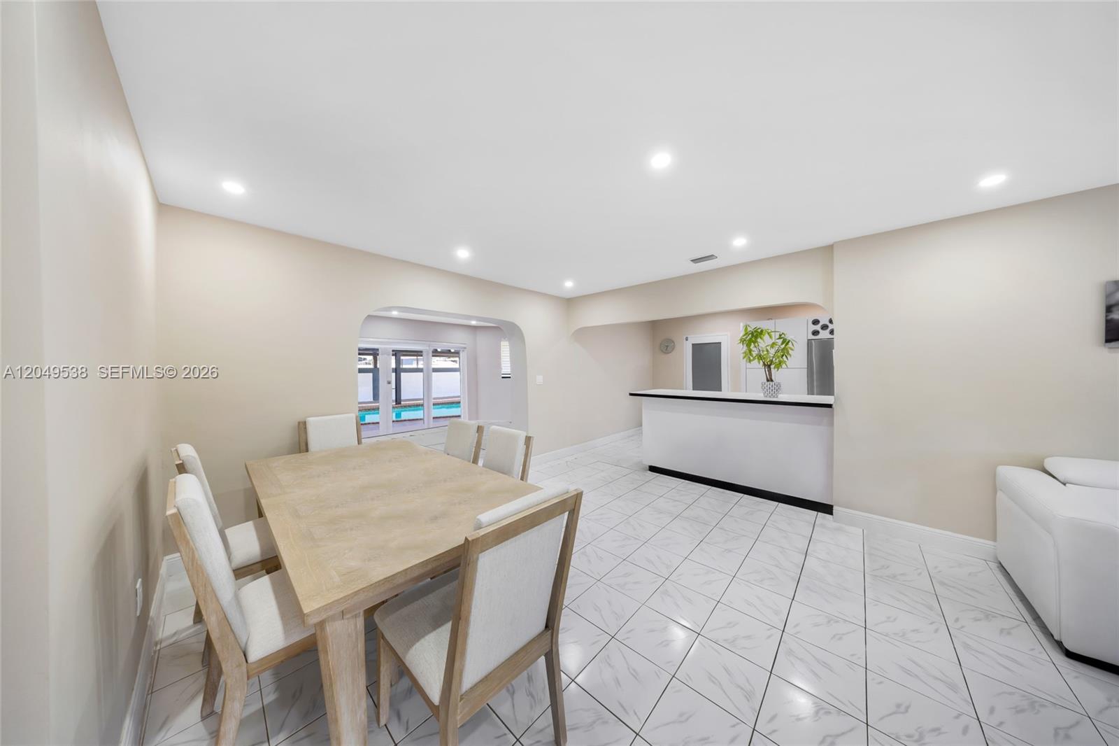 A dining area with a wooden table and chairs leads to a bar and patio — 490 W 33rd Pl, Hialeah FL 33012, HIALEAH, FL