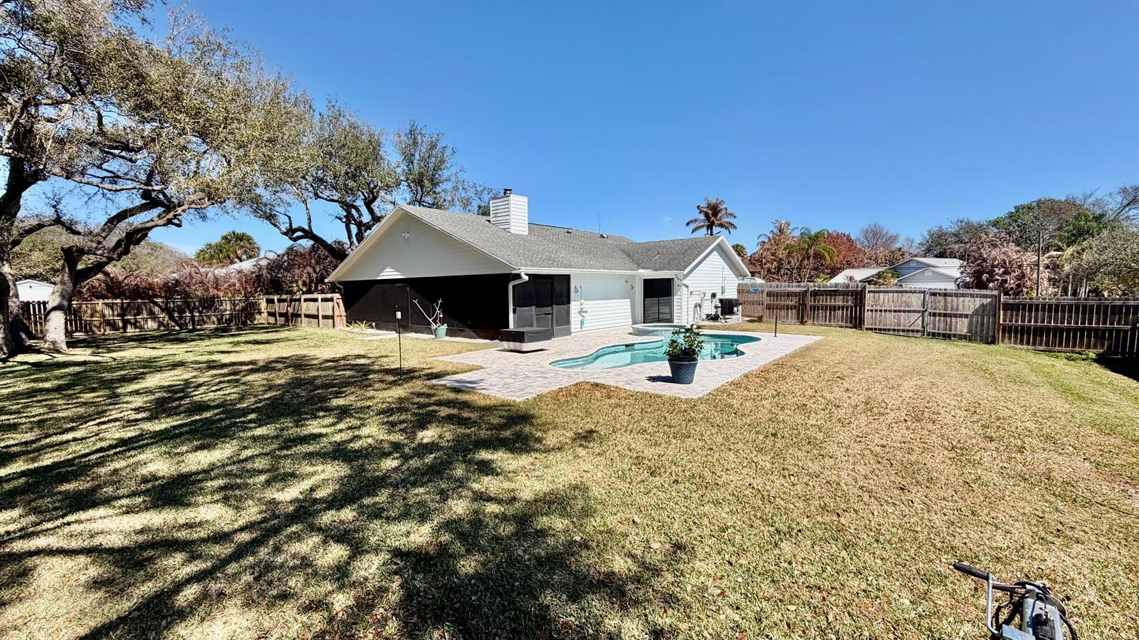 A backyard features a swimming pool, a paved patio, and a white house with a chimney — 311 Anchor Way, FL 34946, FL