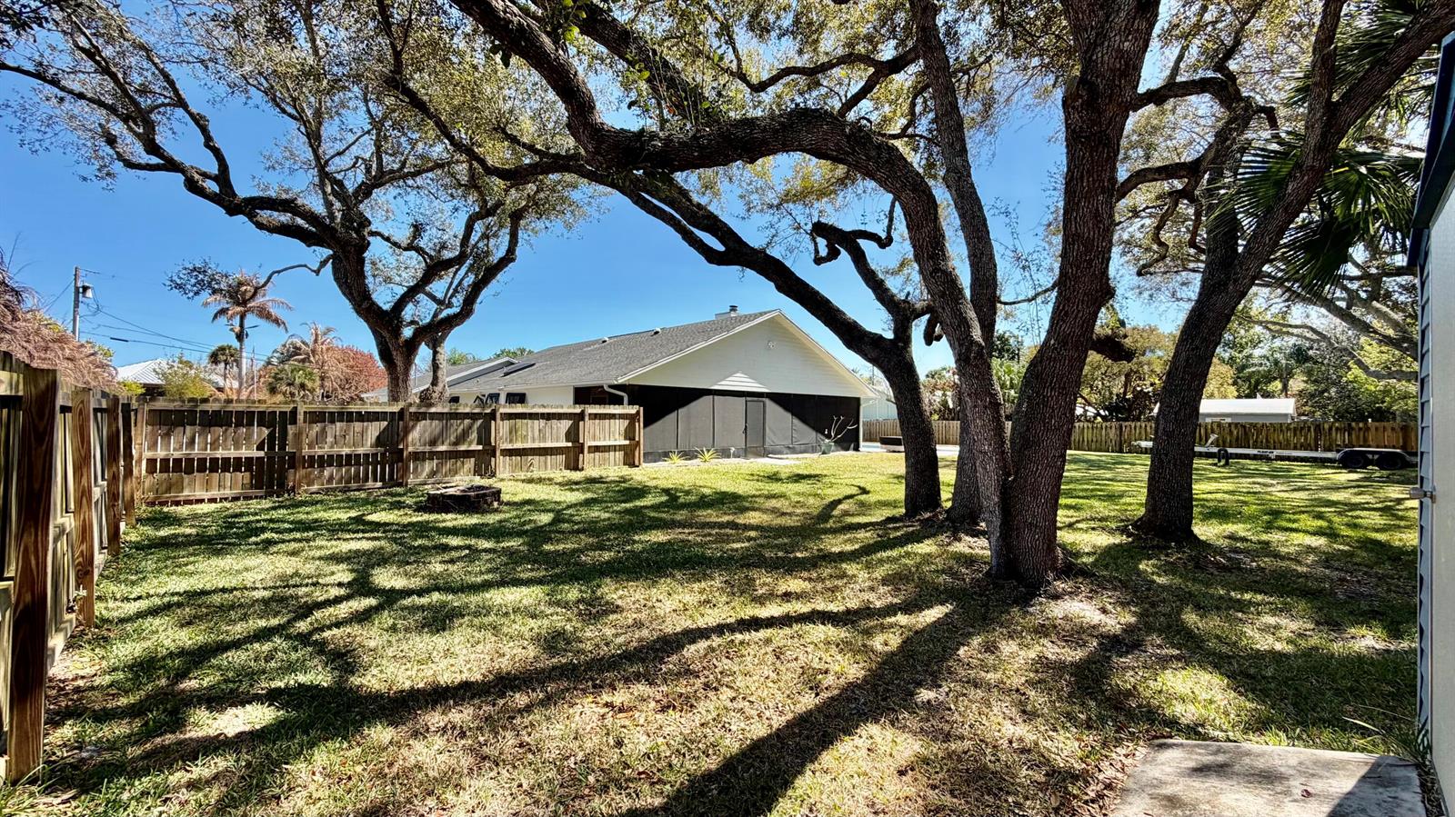 A grassy backyard features large oak trees, a wooden fence, and a screened-in patio area — 311 Anchor Way, FL 34946, FL
