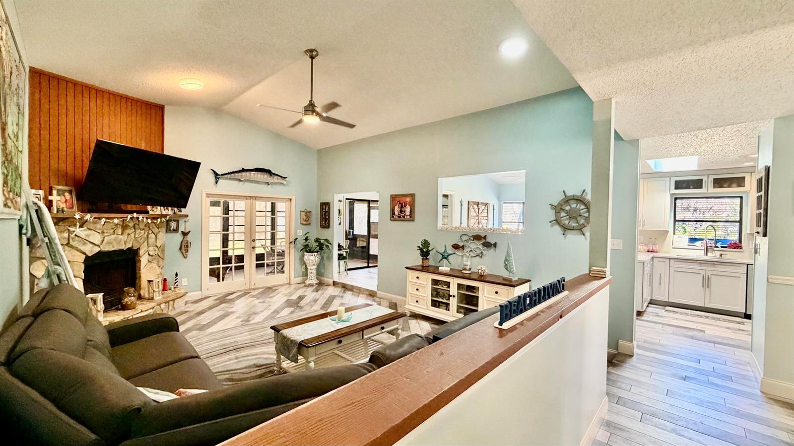 A living room with a stone fireplace, wood-paneled wall, and an adjacent kitchen area — 311 Anchor Way, FL 34946, FL