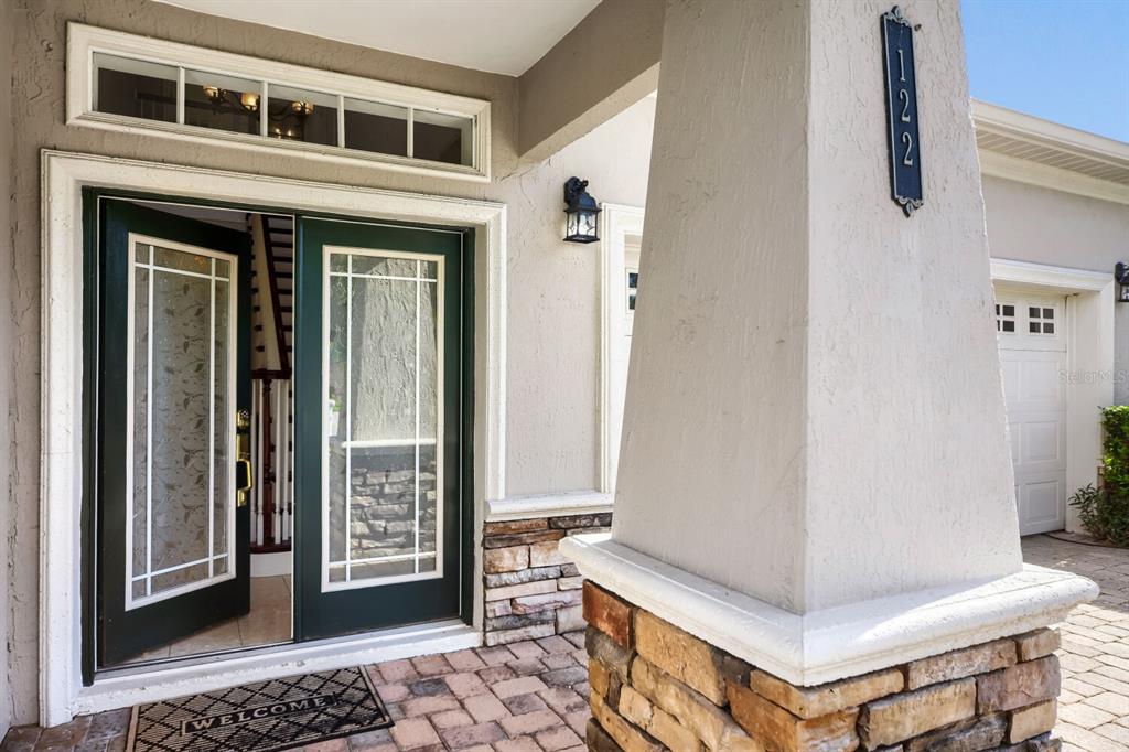 A front entryway with a dark green door, stone pillar, and a brick paver porch — 122 SOPHIA MARIE CV, SANFORD, FL