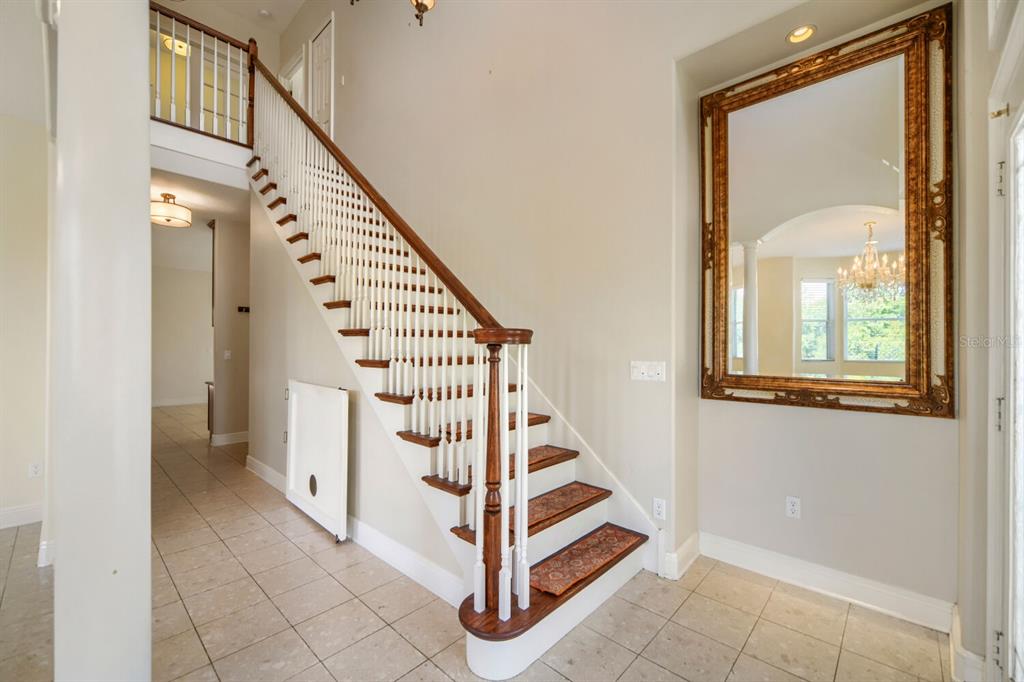 A foyer features a wooden staircase with white balusters, tiled flooring, and a large wall mirror — 122 SOPHIA MARIE CV, SANFORD, FL