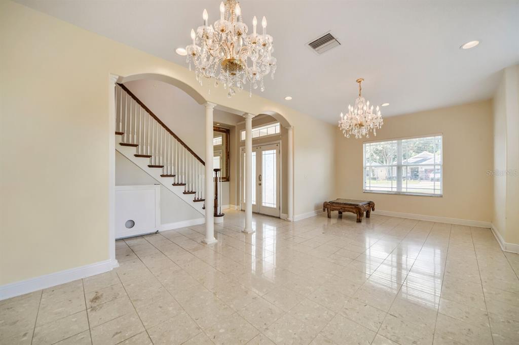 A bright foyer features tile flooring, two crystal chandeliers, a staircase, and a front door — 122 SOPHIA MARIE CV, SANFORD, FL