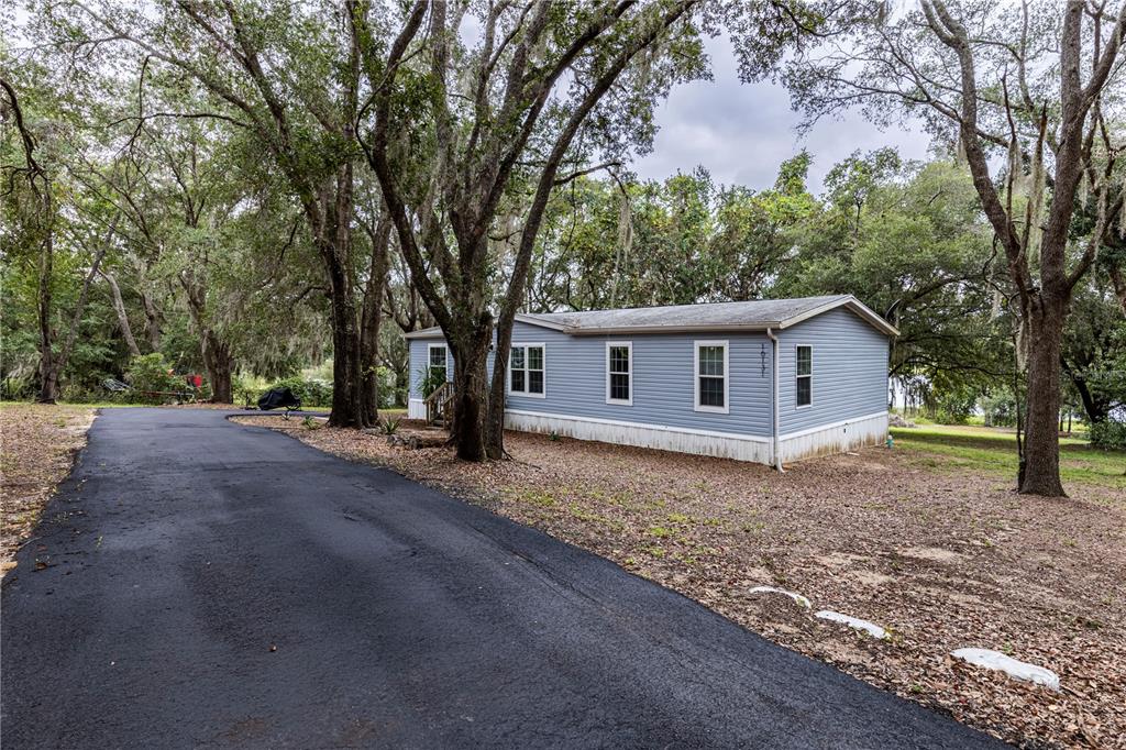 A blue manufactured home sits on a wooded lot next to a paved driveway — 10135 N EM EN EL GROVE ROAD, LEESBURG, FL