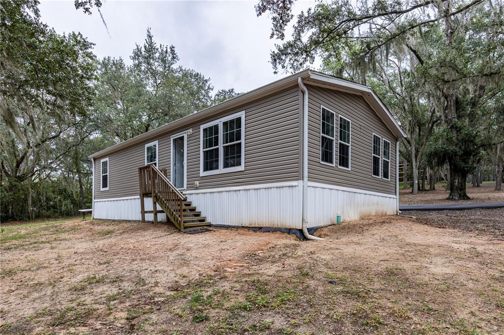 A tan manufactured home with white skirting and wooden stairs sits on a dirt lot — 10135 N EM EN EL GROVE ROAD, LEESBURG, FL