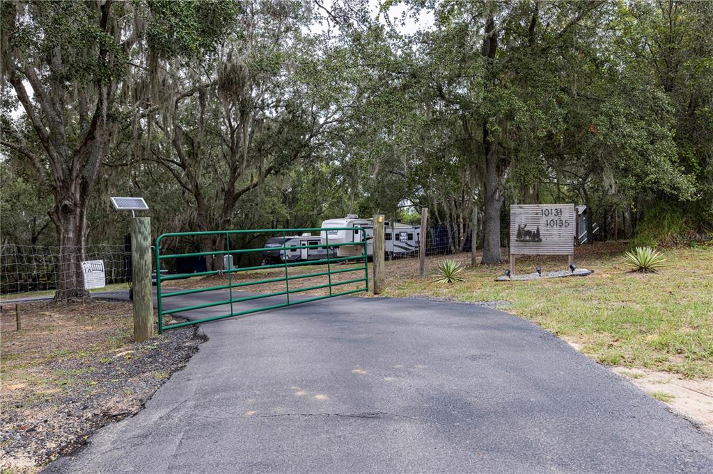 A green metal gate blocks a paved driveway leading to a parked recreational vehicle — 10135 N EM EN EL GROVE ROAD, LEESBURG, FL