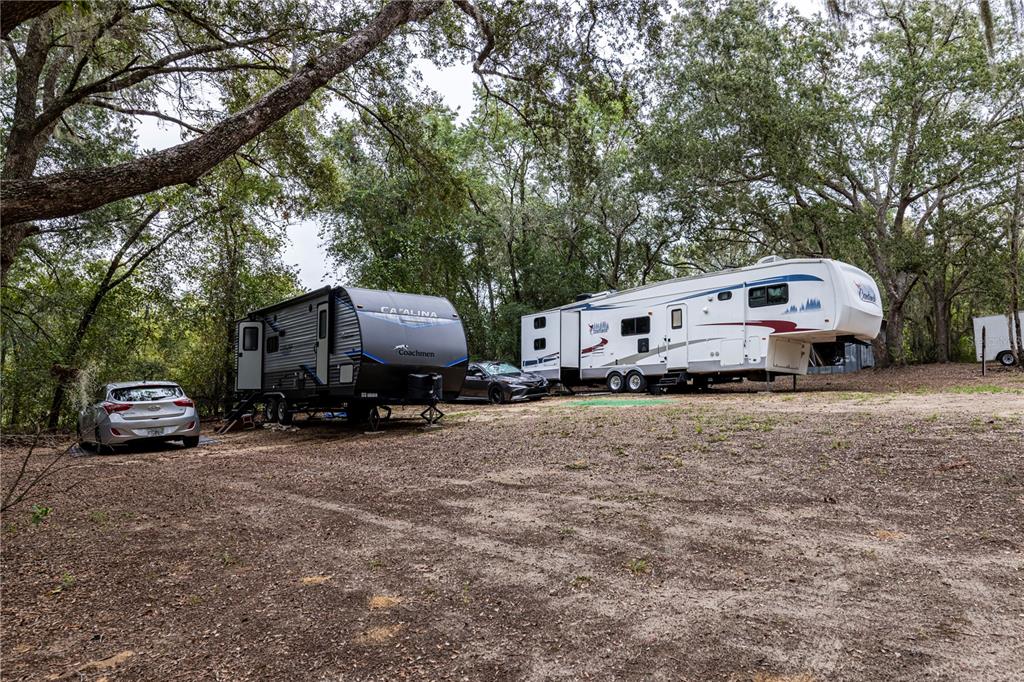 Two recreational vehicles are parked on a dirt lot surrounded by trees — 10135 N EM EN EL GROVE ROAD, LEESBURG, FL