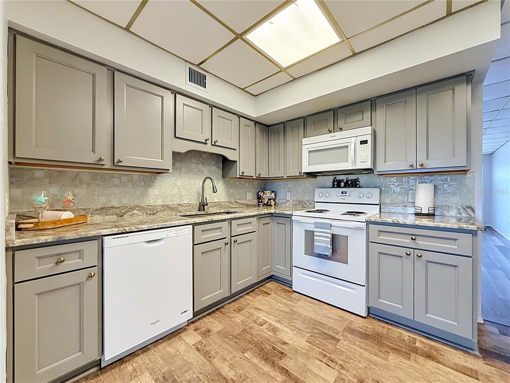 A kitchen features gray cabinets, white appliances, a tiled backsplash, and wood-look flooring — 5860 43RD TERRACE N UNIT 1513, KENNETH CITY, FL