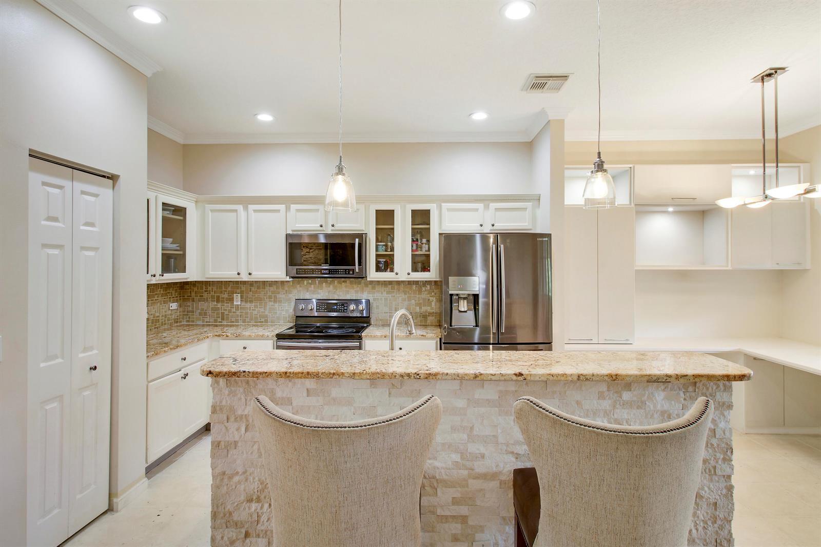 A kitchen features white cabinetry, granite countertops, stainless steel appliances, and a stone-faced breakfast bar — 1448 Artimino Lane, Boynton Beach FL 33436, BOYNTON BEACH, FL