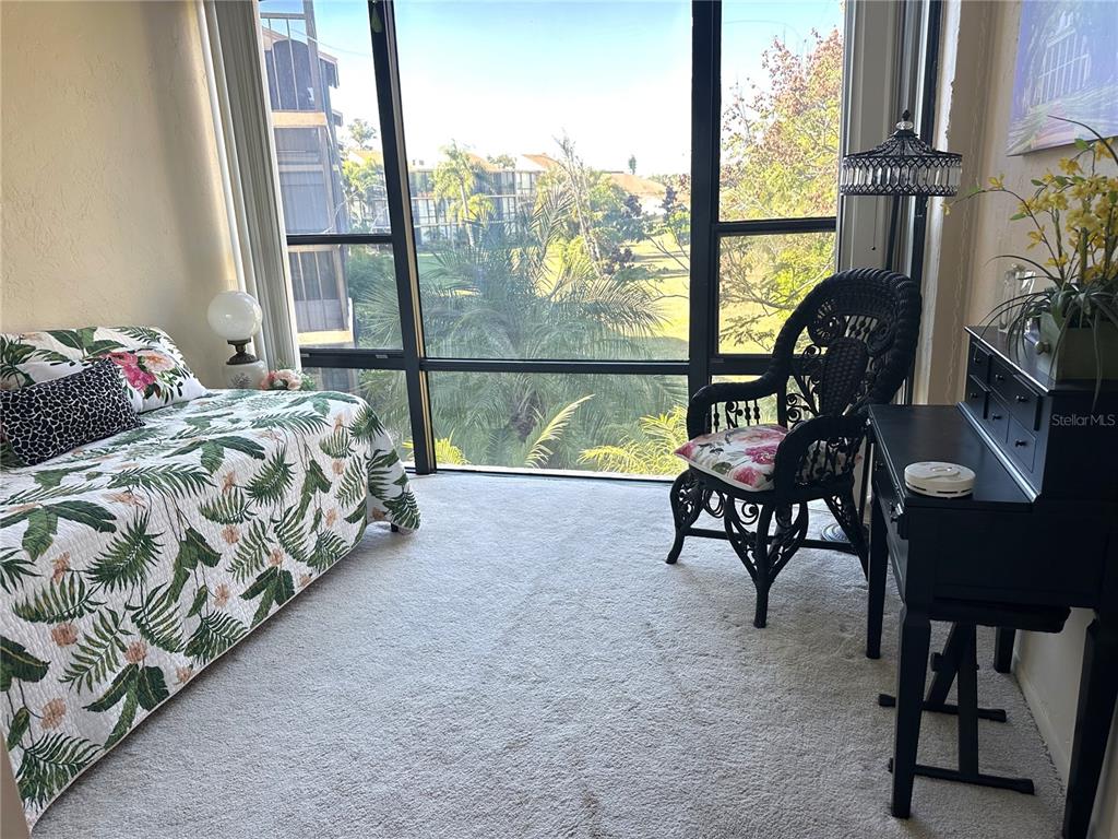 A bedroom features a bed with a tropical quilt, a wicker chair, and large windows — 618 BIRD BAY DRIVE S UNIT 201, VENICE, FL