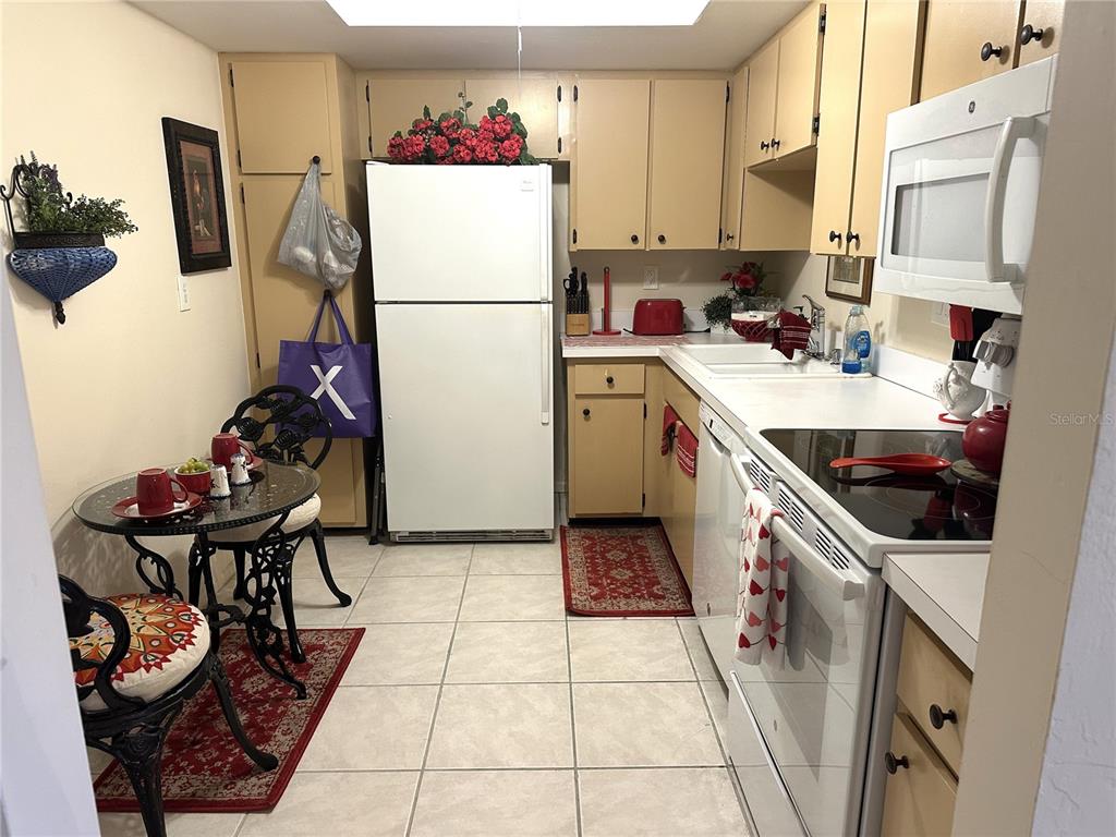 A kitchen features white appliances, light-colored cabinetry, tile flooring, and a small dining table — 618 BIRD BAY DRIVE S UNIT 201, VENICE, FL