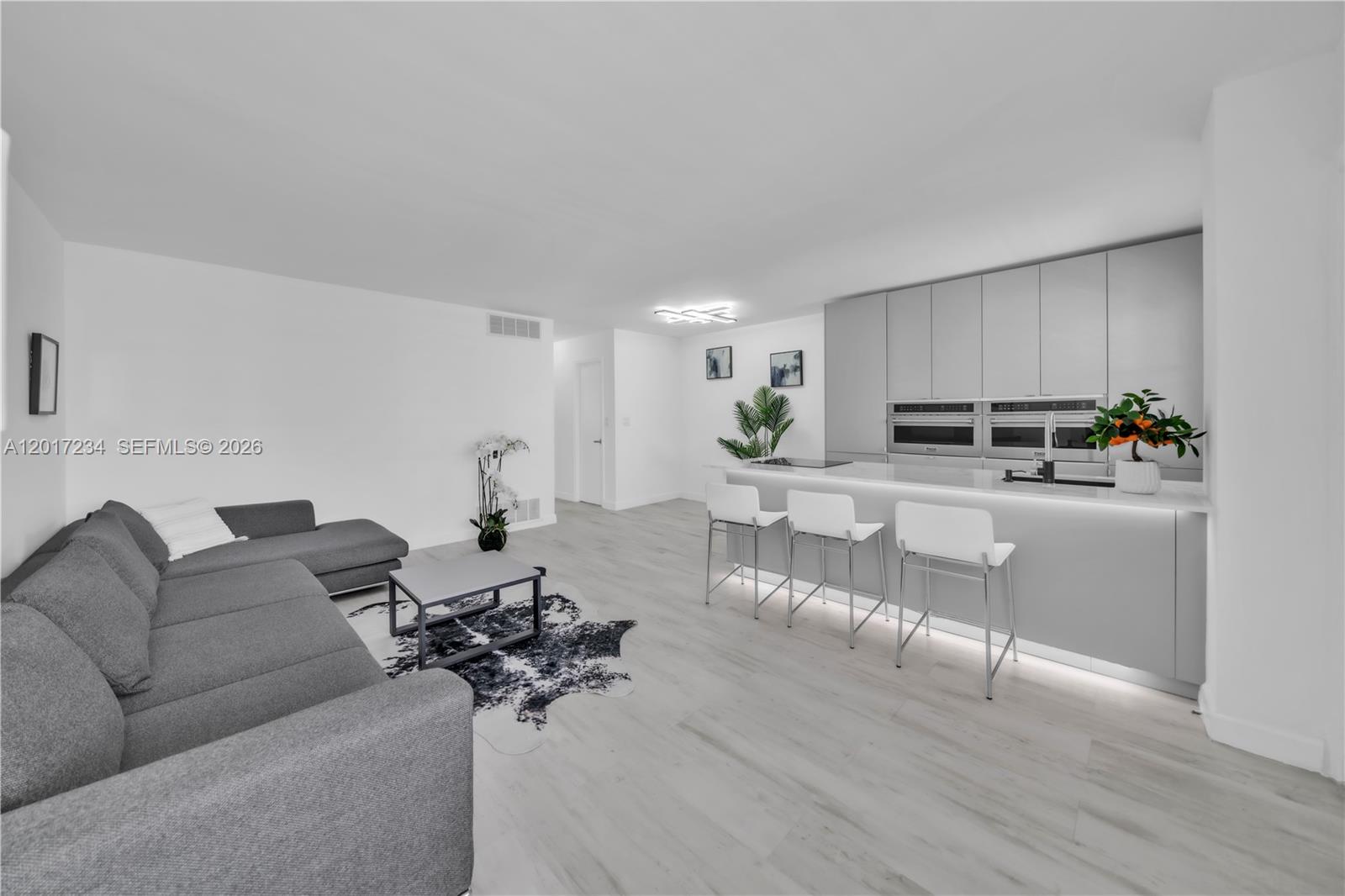 A modern open-concept living room and kitchen featuring gray cabinetry, white bar stools, and flooring — 1720 Jefferson St # 511, Hollywood FL 33020, HOLLYWOOD, FL