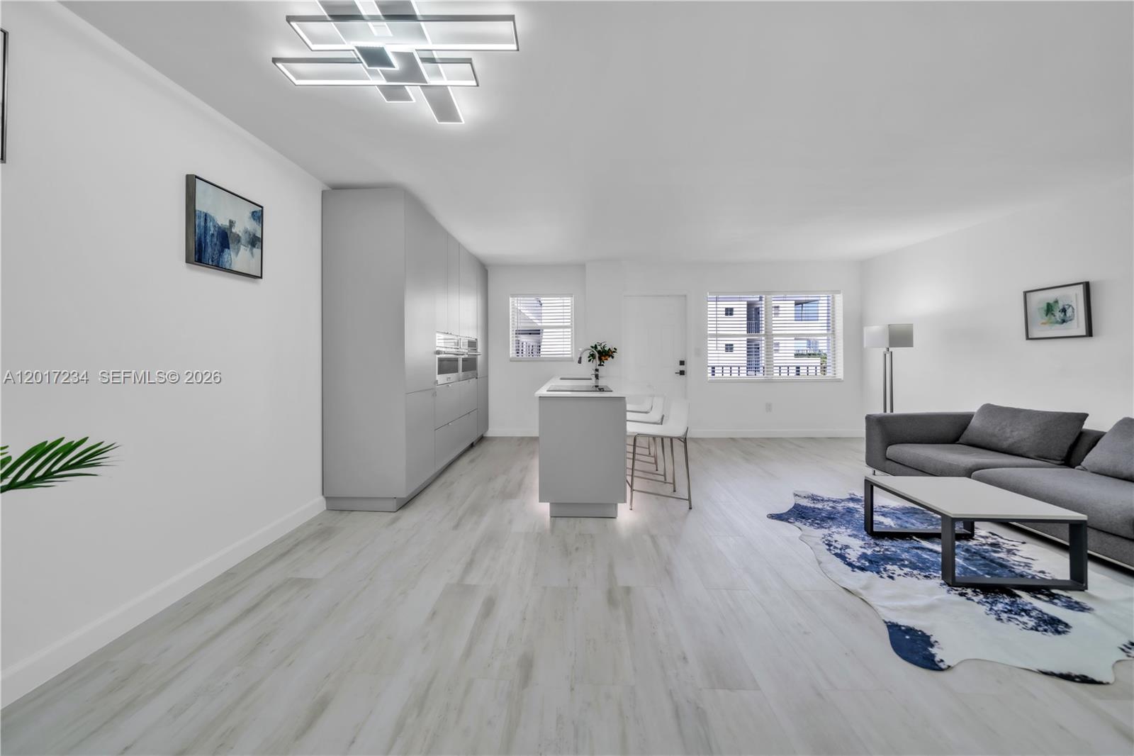 A modern open-concept living area features a kitchen island, gray cabinetry, and light wood flooring — 1720 Jefferson St # 511, Hollywood FL 33020, HOLLYWOOD, FL