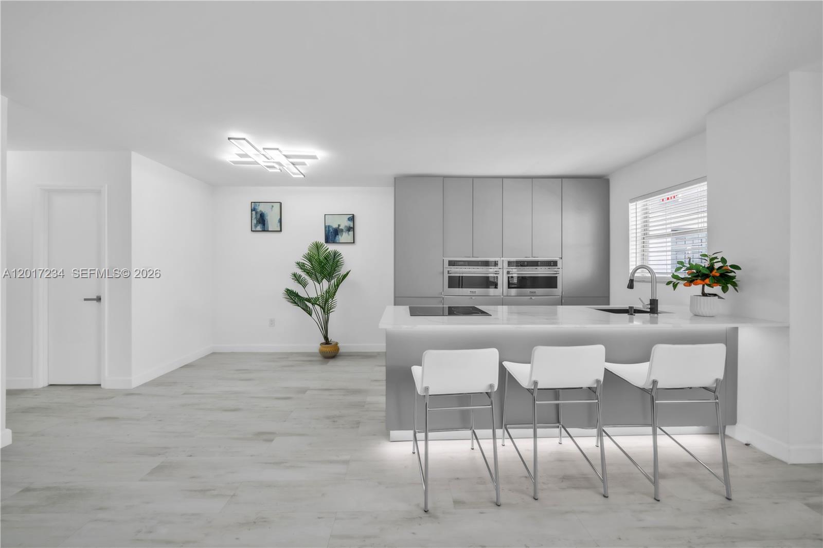 A modern kitchen features gray cabinetry, a white island with bar stools, and light flooring — 1720 Jefferson St # 511, Hollywood FL 33020, HOLLYWOOD, FL