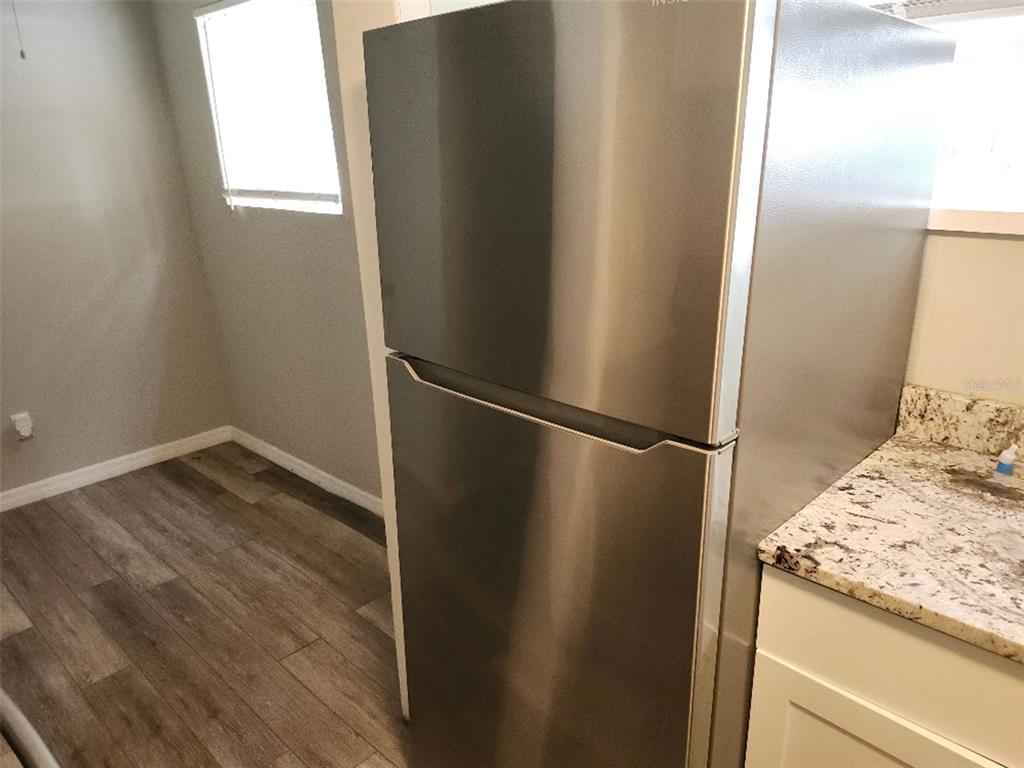 A stainless steel top-freezer refrigerator stands in a kitchen with wood-look flooring and granite countertops — 1426 10TH STREET W, BRADENTON, FL