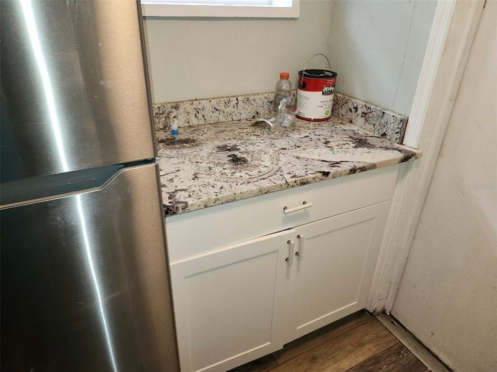A kitchen corner features white cabinets, a granite countertop, and a stainless steel refrigerator — 1426 10TH STREET W, BRADENTON, FL
