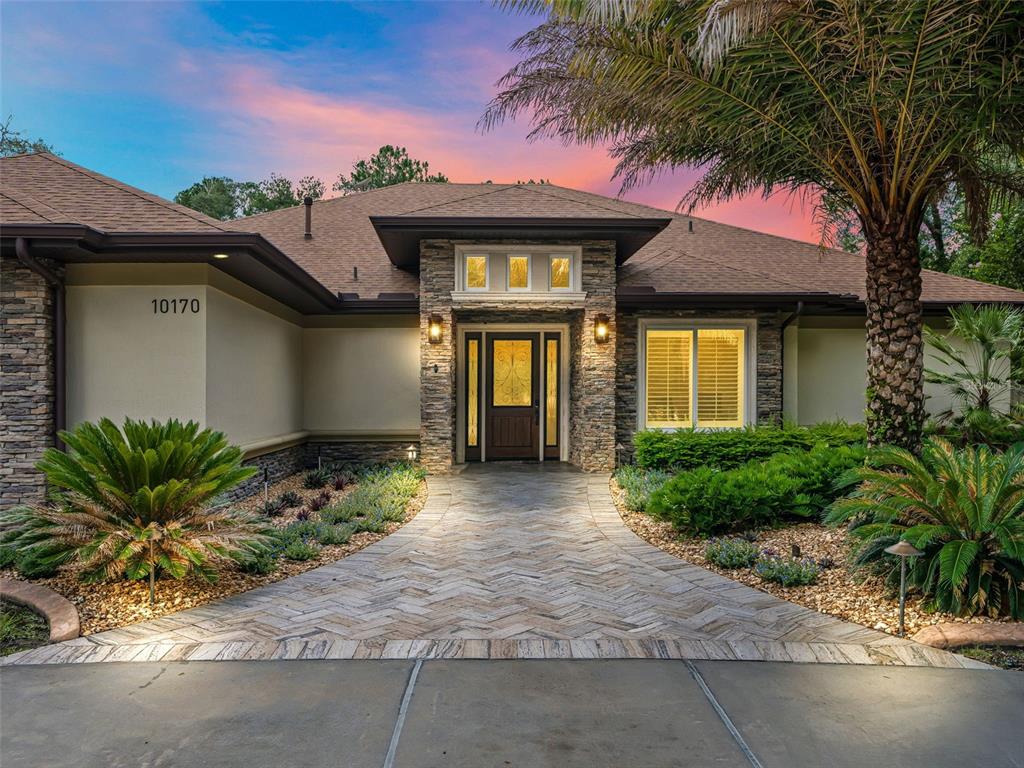 A single-story house exterior features a stone facade, a herringbone paver walkway, and a palm tree — 10170 SW 202ND CIRCLE, DUNNELLON, FL