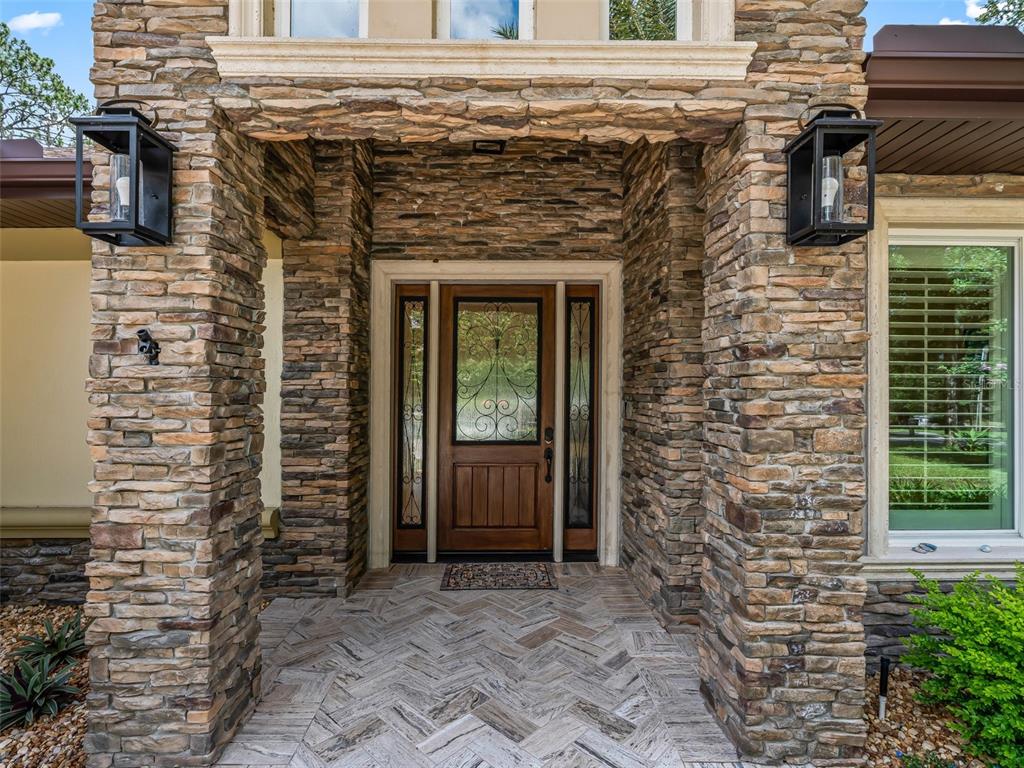 A stone-clad entryway features a wooden front door with glass sidelights and herringbone tile flooring — 10170 SW 202ND CIRCLE, DUNNELLON, FL