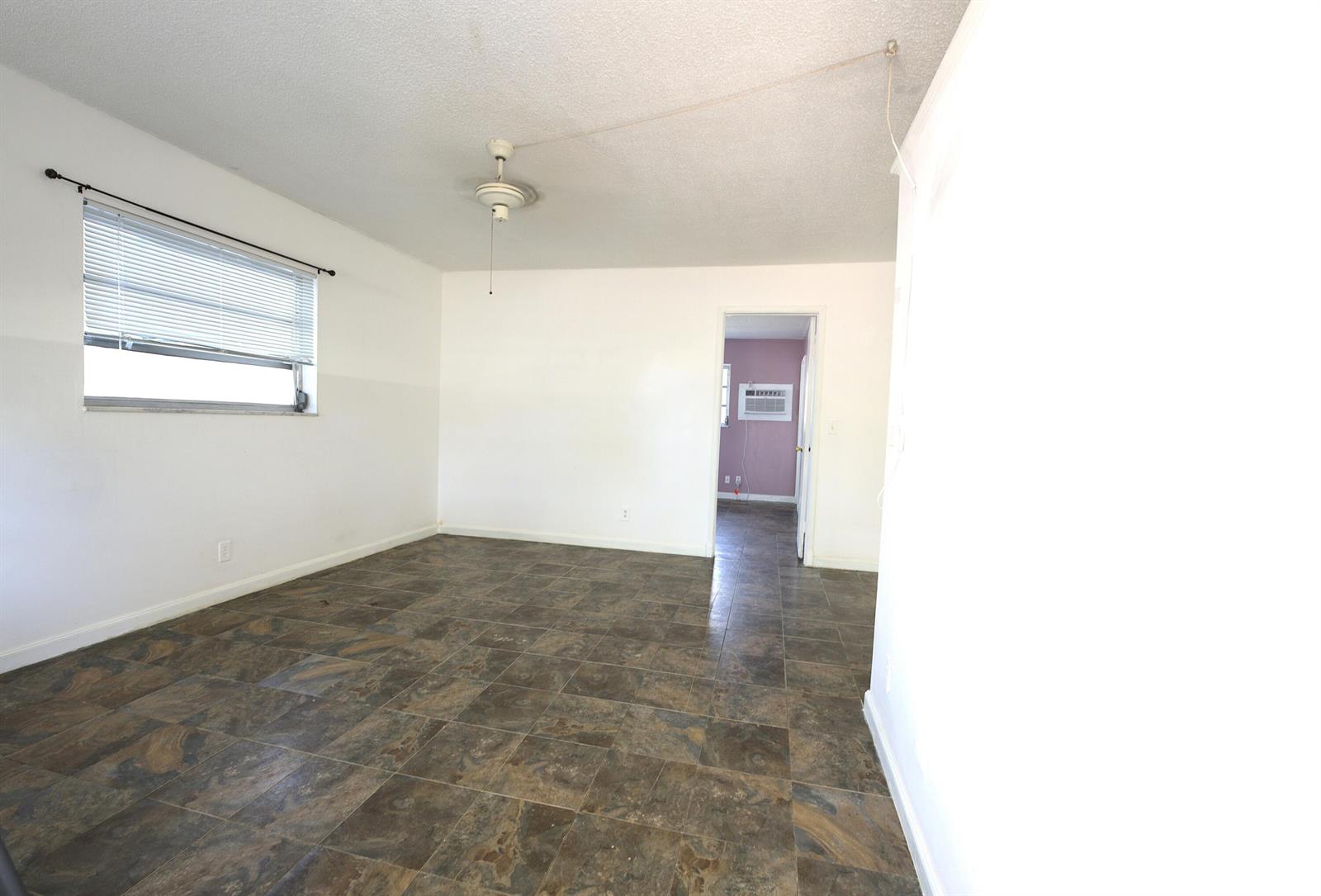 An empty room features white walls, dark tile flooring, a ceiling fan, and a window — 220 Lucerne Avenue # 1, FL 33460, FL