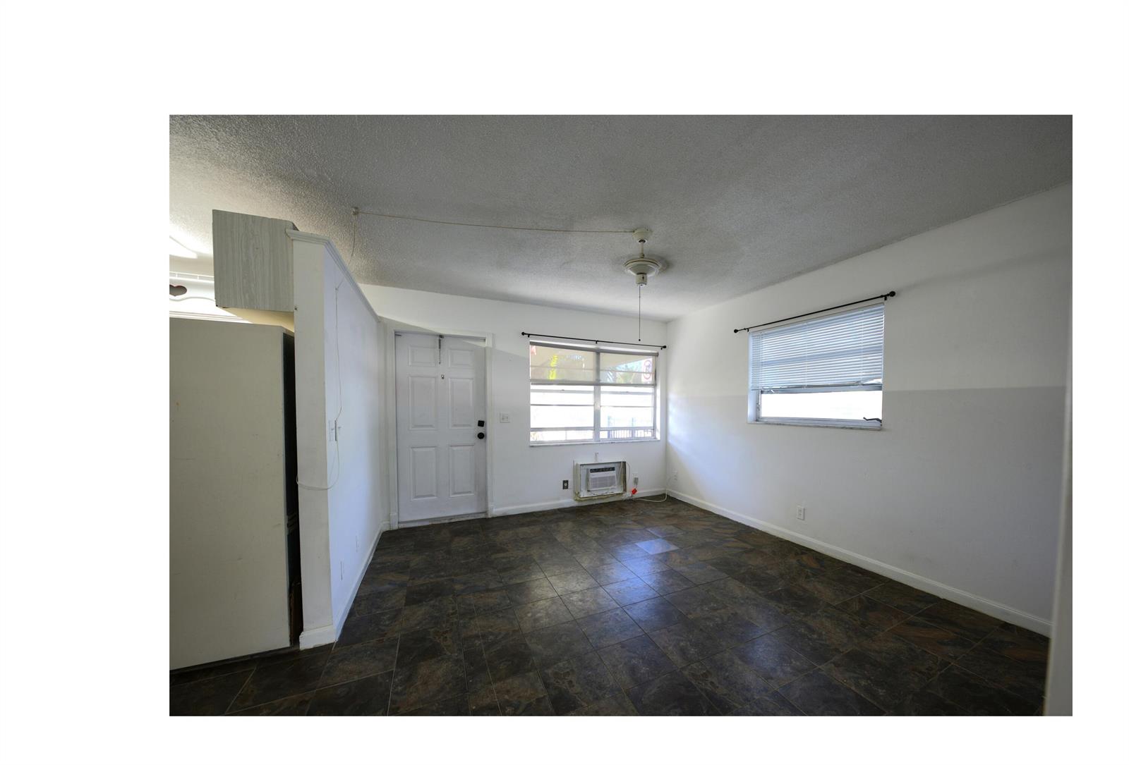 An empty room features dark tile flooring, white walls, two windows, and a white door — 220 Lucerne Avenue # 1, FL 33460, FL