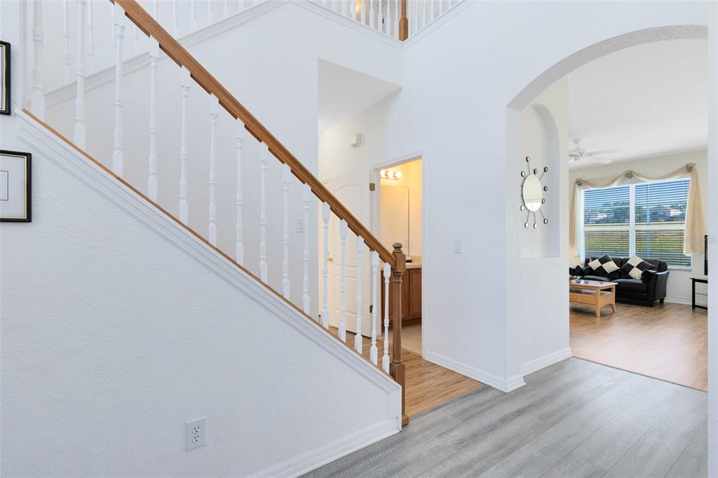 A foyer with a staircase, wood-look flooring, and an arched entryway leading to a living room — 142 BIRKDALE STREET, DAVENPORT, FL