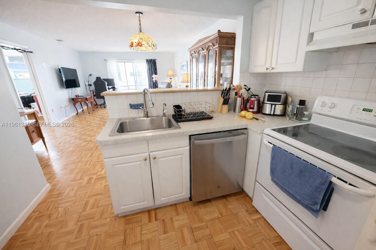 A kitchen with white cabinets, stainless steel appliances, and parquet flooring overlooks a living area — 16750 NE 14th Ave # 202, Miami FL 33162, MIAMI, FL