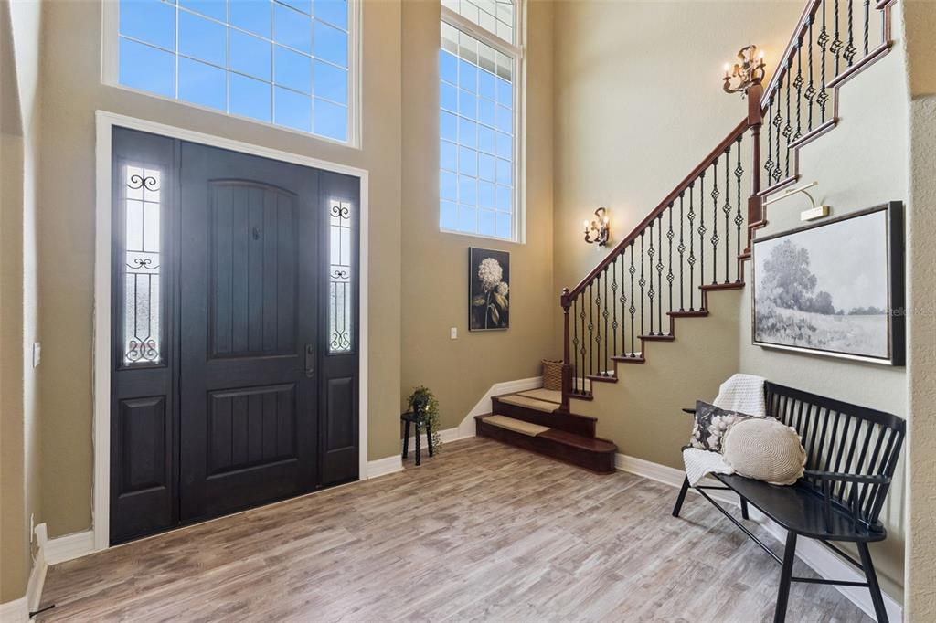 A bright entryway features a dark front door, a staircase with iron railings, and wood-look flooring — 4282 MCKINNON ROAD, WINDERMERE, FL