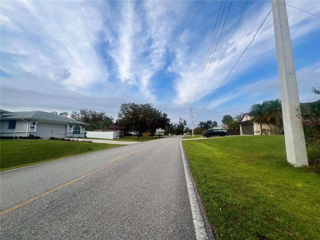 A paved residential street leads toward houses under a blue sky with scattered clouds — 1088 INVERNESS STREET, PORT CHARLOTTE, FL
