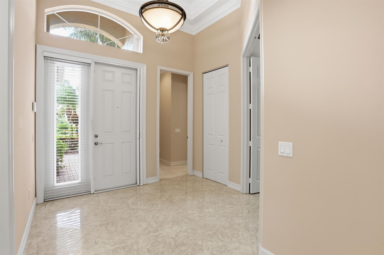 A bright entryway features a front door with a sidelight, tile flooring, and a chandelier — 10825 Leaf Bridge Way, Boynton Beach FL 33473, BOYNTON BEACH, FL