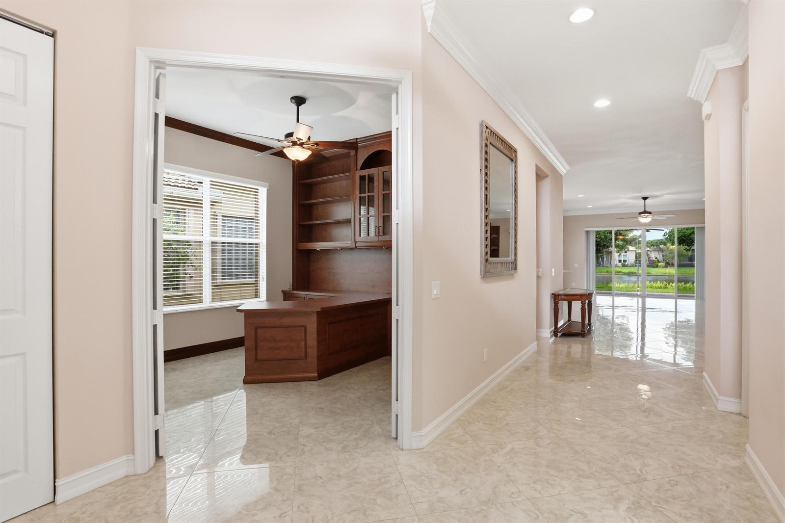 A view from a hallway into a home office with built-in wooden cabinetry and desks — 10825 Leaf Bridge Way, Boynton Beach FL 33473, BOYNTON BEACH, FL