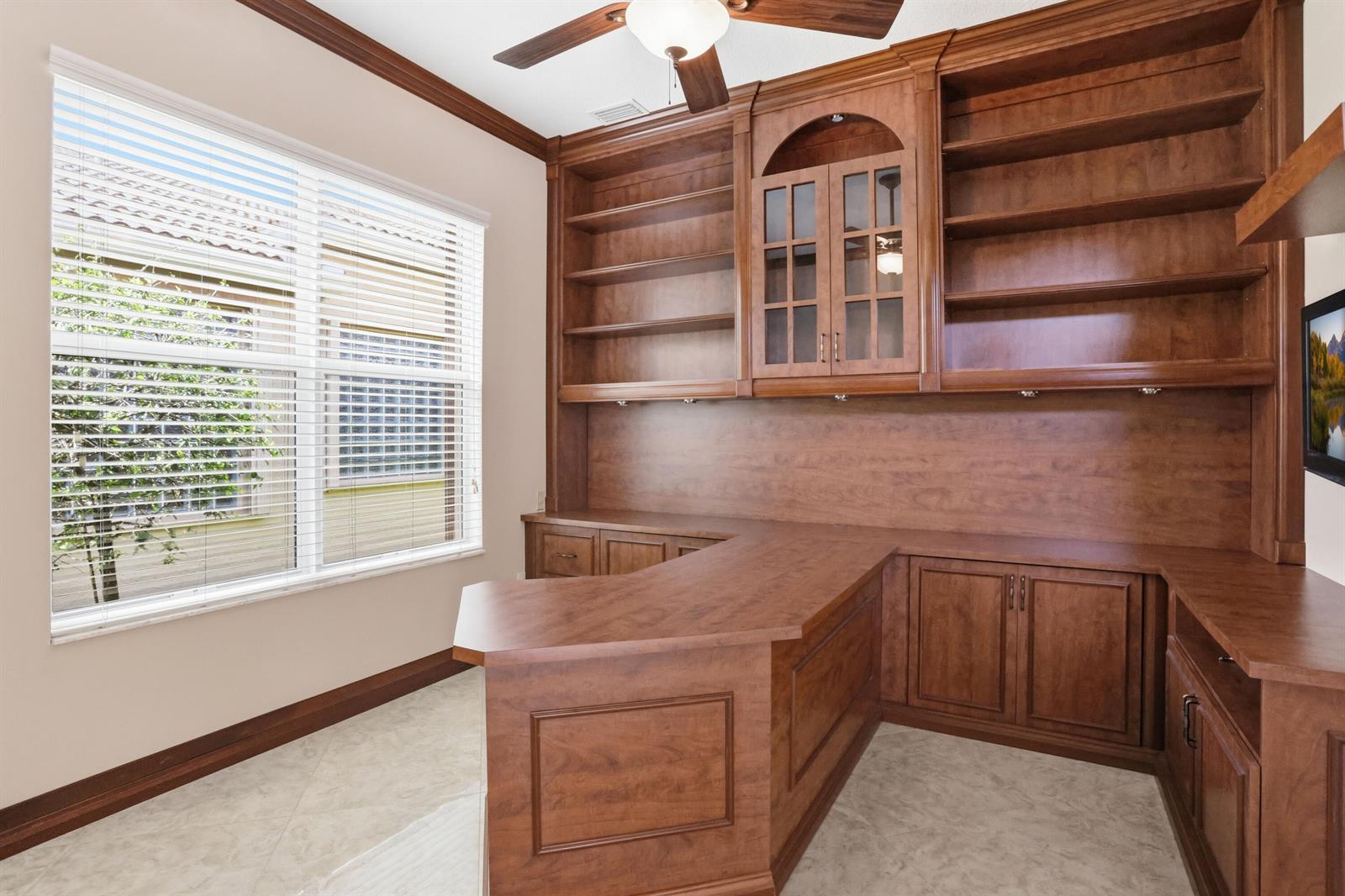 A home office features a large L-shaped wooden desk, built-in shelving, and a window — 10825 Leaf Bridge Way, Boynton Beach FL 33473, BOYNTON BEACH, FL