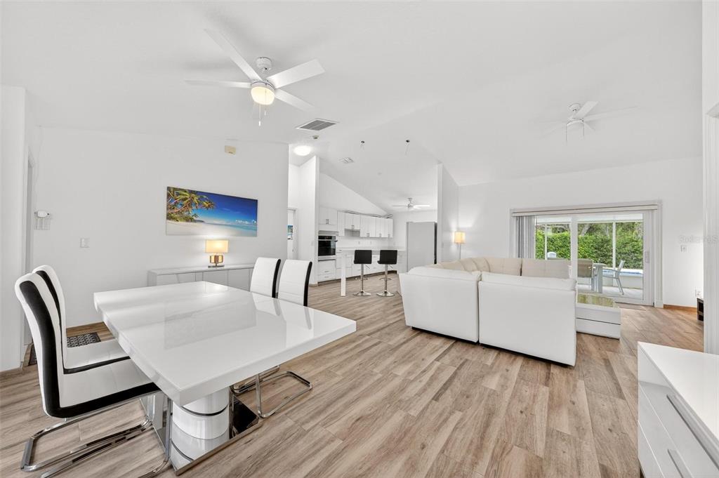 An open-concept living and dining area features white furniture, wood-look flooring, and a vaulted ceiling — 12623 LAKE DENISE BOULEVARD, CLERMONT, FL