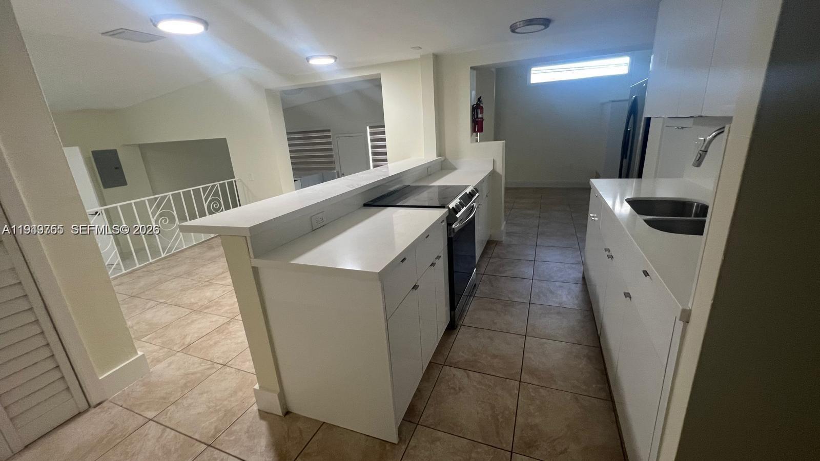 A kitchen with white cabinets and countertops overlooks a living area with tiled floors — 1251 Little River Dr, Miami FL 33147, MIAMI, FL
