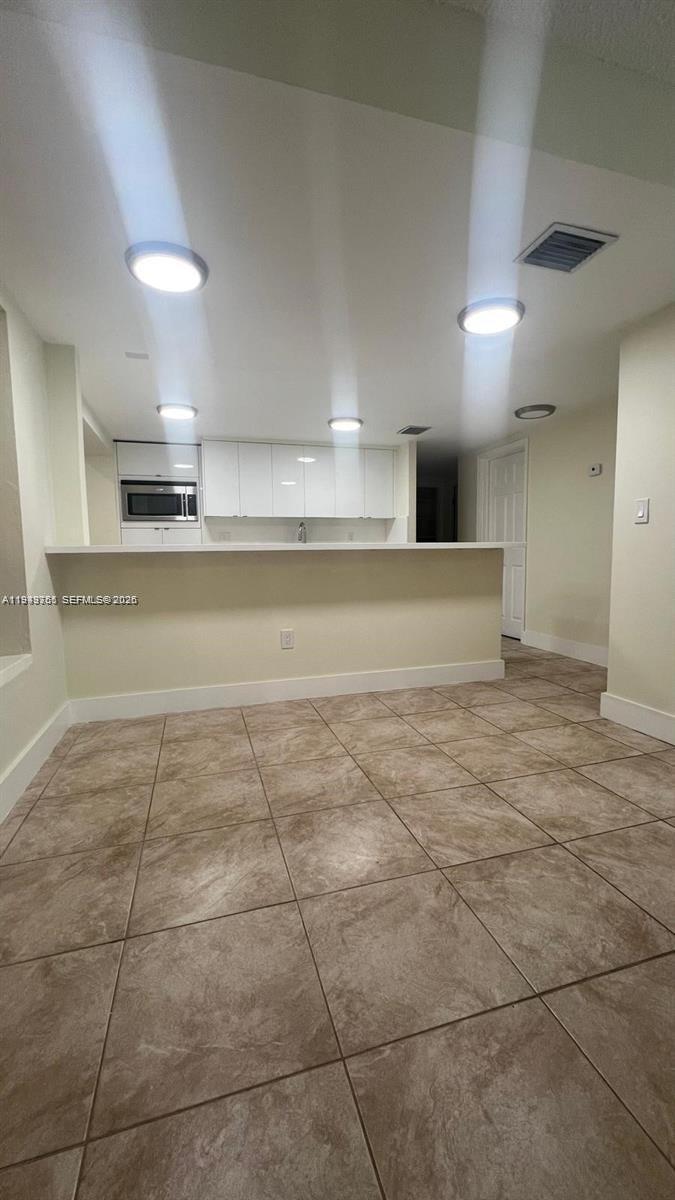 A kitchen with white cabinets and a breakfast bar overlooks a tiled dining area — 1251 Little River Dr, Miami FL 33147, MIAMI, FL