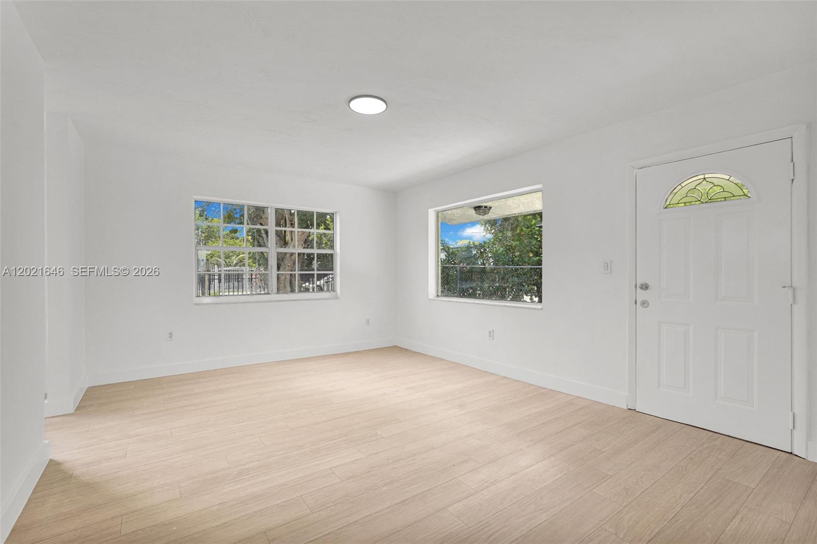 An empty room features white walls, light wood-look flooring, two windows, and a white door — 151 NW 42nd St # 1, Miami FL 33127, MIAMI, FL