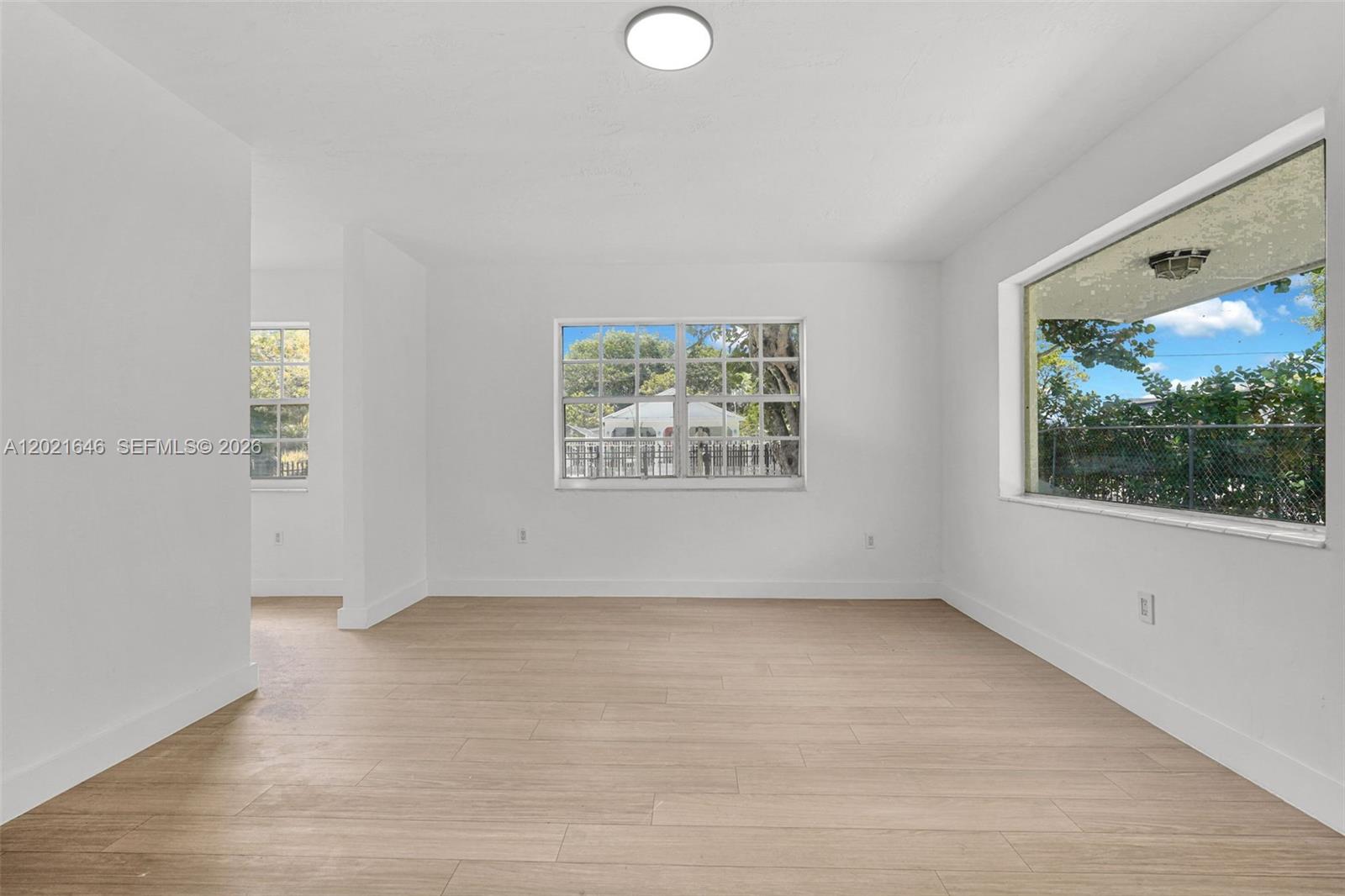 An empty room features white walls, light wood-look flooring, and several windows overlooking a yard — 151 NW 42nd St # 1, Miami FL 33127, MIAMI, FL