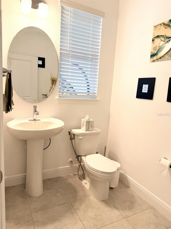 A half bathroom features a pedestal sink, oval mirror, toilet, and light-colored tile flooring — 16435 HAMLIN HILLS ROAD, WINTER GARDEN, FL