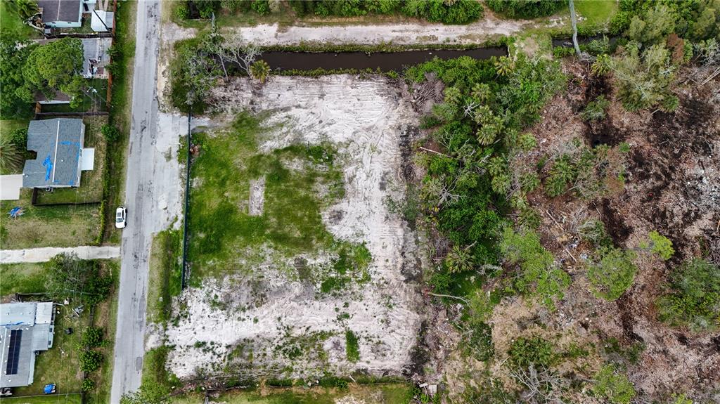 An aerial view shows a cleared, sandy residential lot bordered by a road and vegetation — 6644 OELSNER STREET, NEW PORT RICHEY, FL