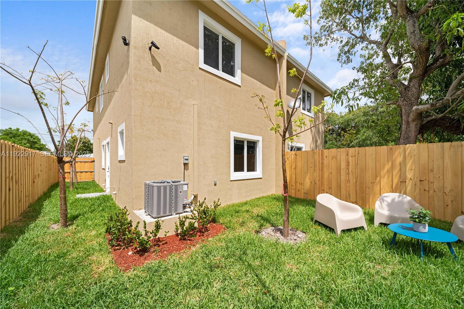 A tan two-story house exterior features a small backyard with a wooden fence and chairs — 1770 NW 55th St, Miami FL 33142, MIAMI, FL