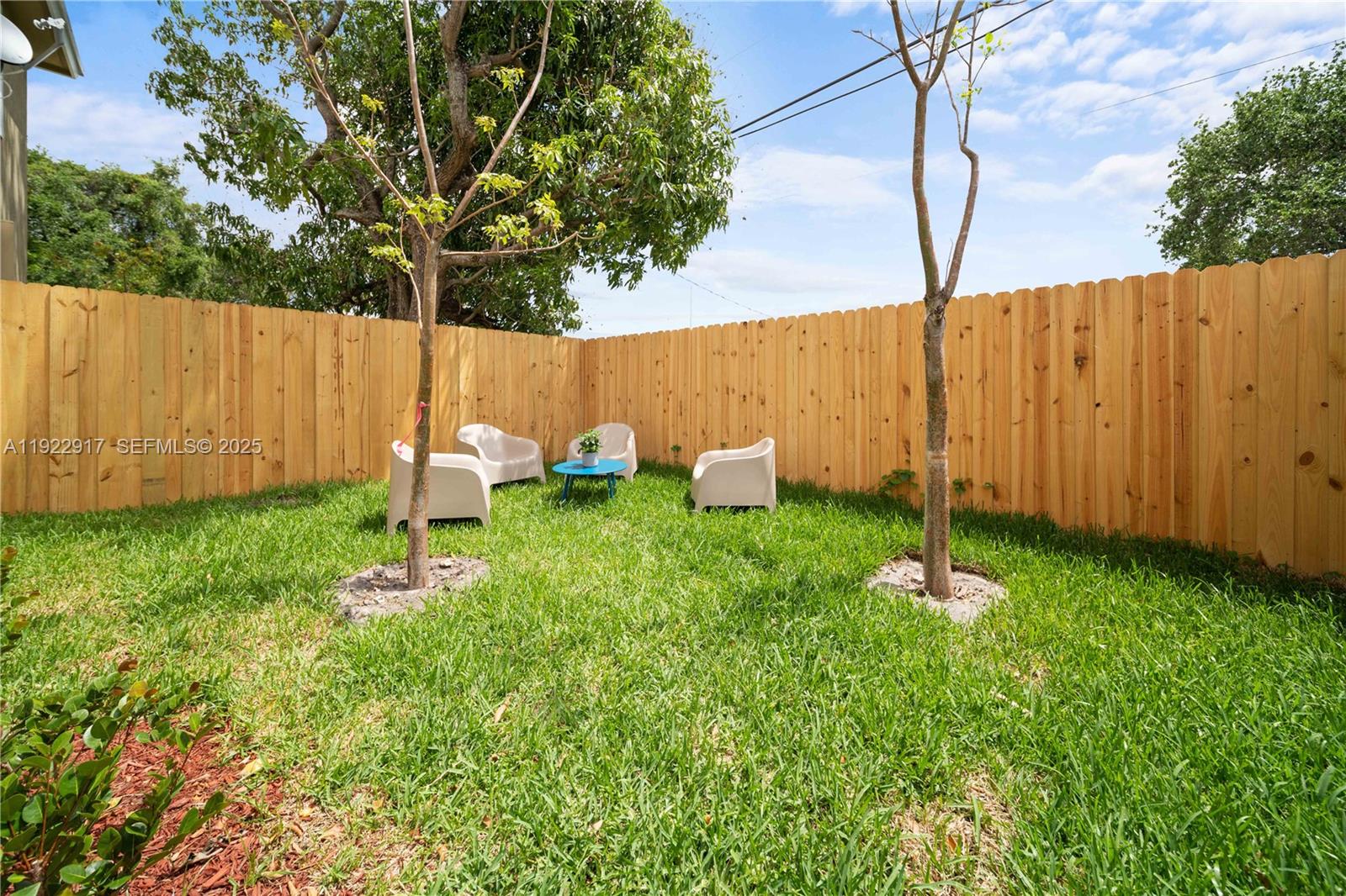 A grassy backyard features a wooden privacy fence, two young trees, and patio furniture — 1770 NW 55th St, Miami FL 33142, MIAMI, FL