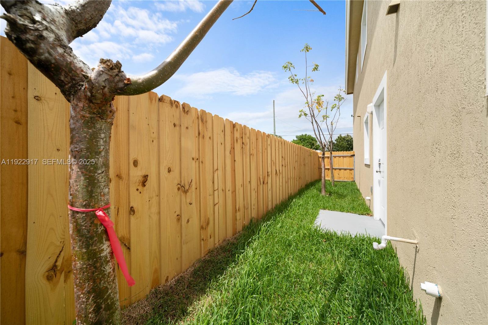 A narrow side yard features a wooden fence, a small tree, and a white door — 1770 NW 55th St, Miami FL 33142, MIAMI, FL