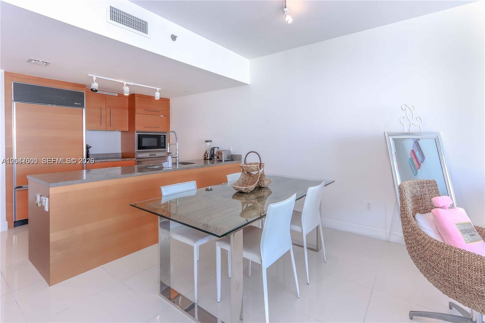 A modern kitchen with wood cabinetry and a glass-topped dining table in an open space — 475 Brickell Ave # 4612, Miami FL 33131, MIAMI, FL