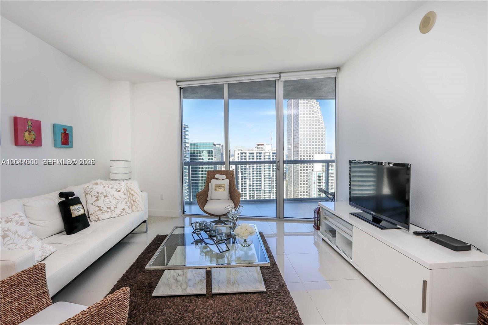 A bright living room features white furniture, a glass coffee table, and floor-to-ceiling city views — 475 Brickell Ave # 4612, Miami FL 33131, MIAMI, FL
