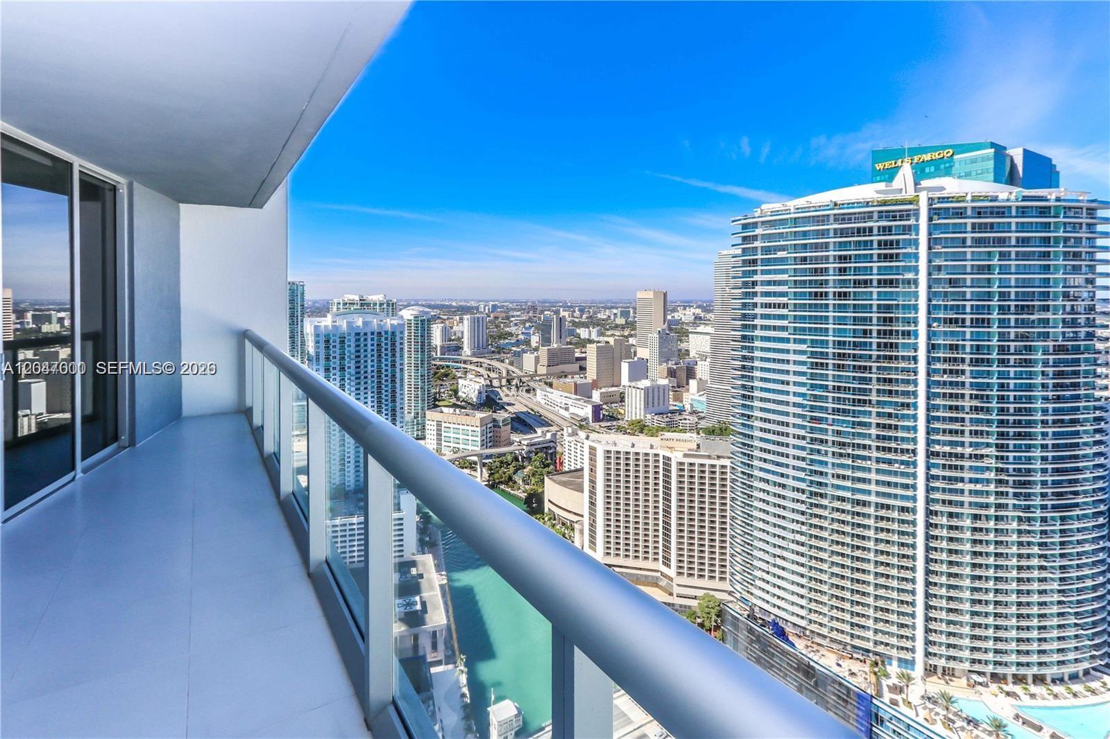 A high-rise balcony overlooks a dense city skyline with a large glass skyscraper nearby — 475 Brickell Ave # 4612, Miami FL 33131, MIAMI, FL