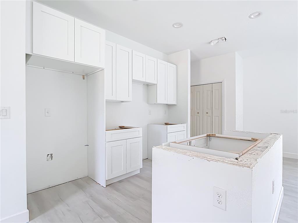 A kitchen under construction features white cabinets, light wood-look flooring, and an unfinished center island — 16134 LIBOURN AVENUE, PORT CHARLOTTE, FL